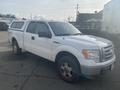 A white 2009 Ford F-150 with a cap on the bed parked on a lot with dirt on the tires and a slightly worn appearance