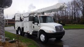 A 2005 International 4300 utility truck with a white exterior and a raised aerial lift attachment mounted on the front