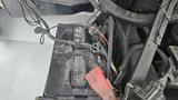 A close-up view of a car battery installed in a 2006 Ford Econoline with several cables connected and some dust visible on the surface