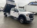 A white 2021 Ford F-550 chassis cab with a raised dump bed, showcasing its large wheels and rugged front design