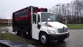 A 2009 Hino 338 garbage truck with a white and black exterior and a red waste container on the back parked at an angle