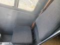 A gray upholstered driver's seat from a 1999 Ford Econoline viewed from above with a flat seat cushion and a sturdy metal frame