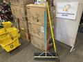 Ten yellow mop buckets stacked beside assorted brooms including a yellow broom with a long handle and a wide dustpan broom