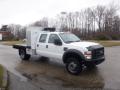 A white 2009 Ford F-450 SD with a flatbed and a utility box in the truck bed featuring a prominent front grille and multiple amber lights on the roof