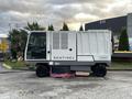 A 2007 Tennant Sentinel street sweeper with a grey body and a white hopper, showcasing its cleaning brushes and branding on the side