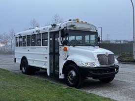 A white 2016 International 4200 school bus with a large front windshield and door on the driver's side, featuring multiple windows along the sides